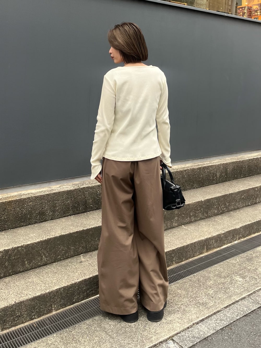 ブラウン系のスラックス、ホワイト系のTシャツ/カットソー、ブラック系のショルダーバッグを着用したレディースの春コーディネートの2枚目の写真