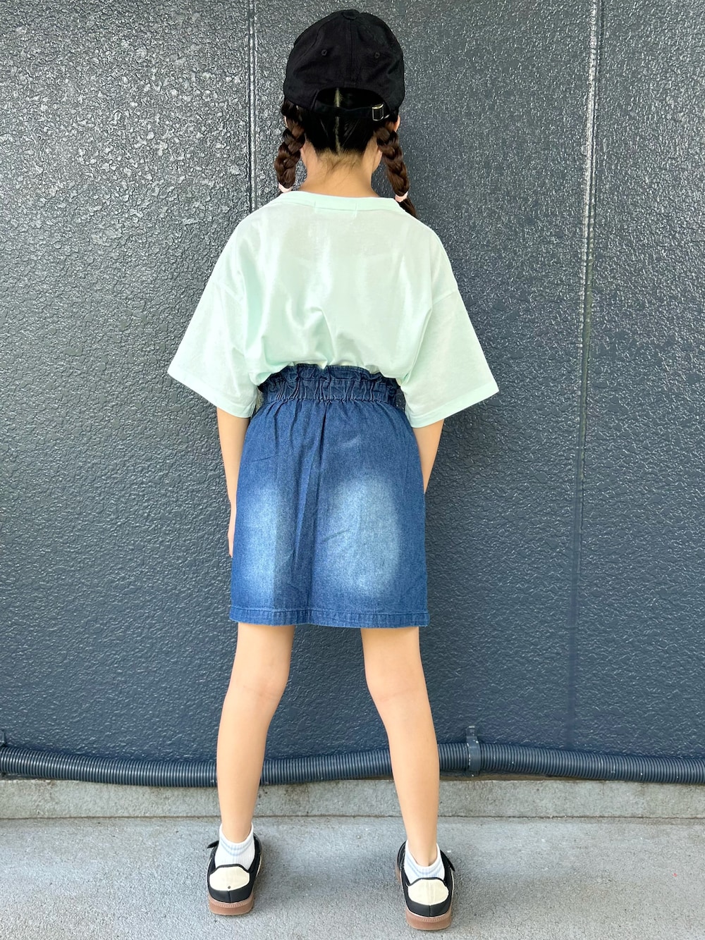グリーン系のTシャツ/カットソー、ブルー系のデニムスカート、ブラック系のキャップを着用したキッズの夏コーディネートの3枚目の写真
