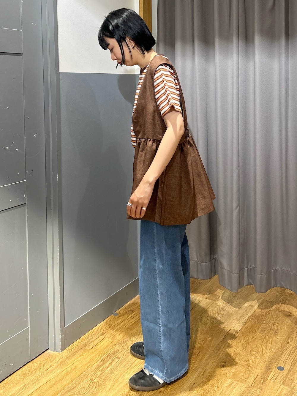 オレンジ系のTシャツ/カットソー、ブラウン系のベスト、ブルー系のデニムパンツを着用したレディースの春コーディネートの3枚目の写真