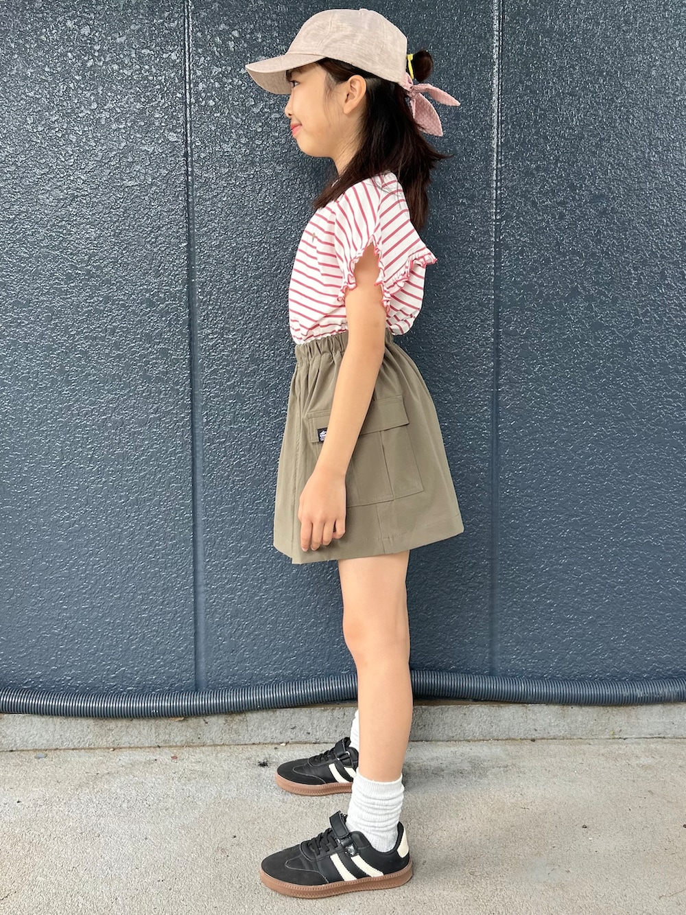 レッド系のTシャツ/カットソー、ブラウン系のスカート、ベージュ系のキャップを着用したキッズの夏コーディネートの2枚目の写真