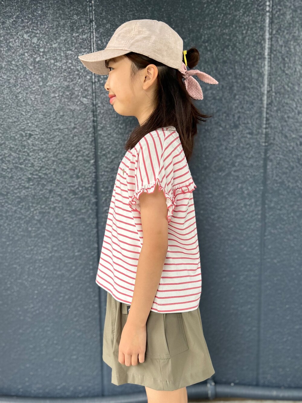 レッド系のTシャツ/カットソー、ブラウン系のスカート、ベージュ系のキャップを着用したキッズの夏コーディネートの7枚目の写真