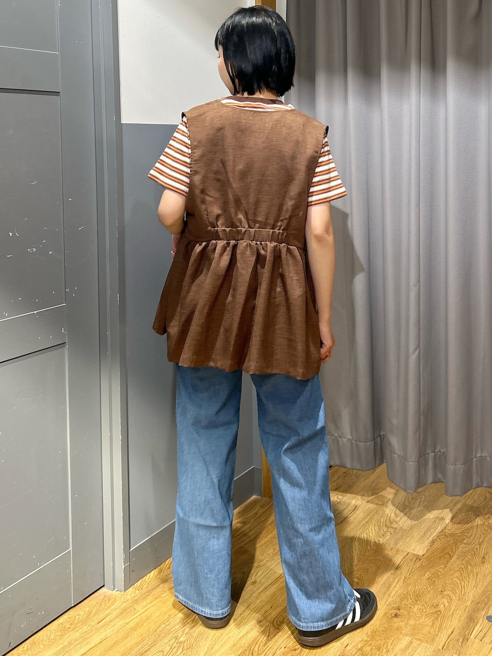 オレンジ系のTシャツ/カットソー、ブラウン系のベスト、ブルー系のデニムパンツを着用したレディースの春コーディネートの4枚目の写真