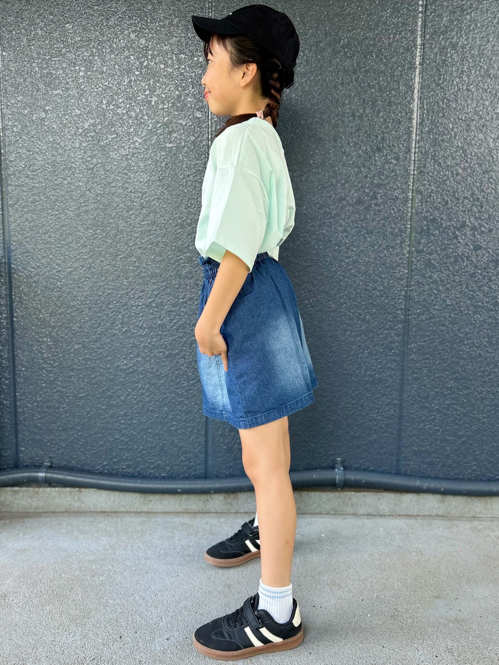 グリーン系のTシャツ/カットソー、ブルー系のデニムスカート、ブラック系のキャップを着用したキッズの夏コーディネートの2枚目の写真