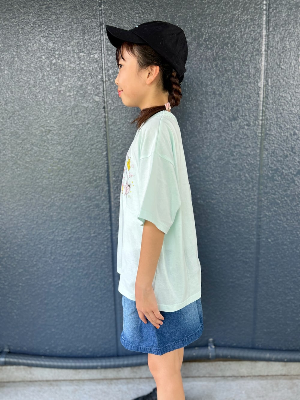 グリーン系のTシャツ/カットソー、ブルー系のデニムスカート、ブラック系のキャップを着用したキッズの夏コーディネートの5枚目の写真