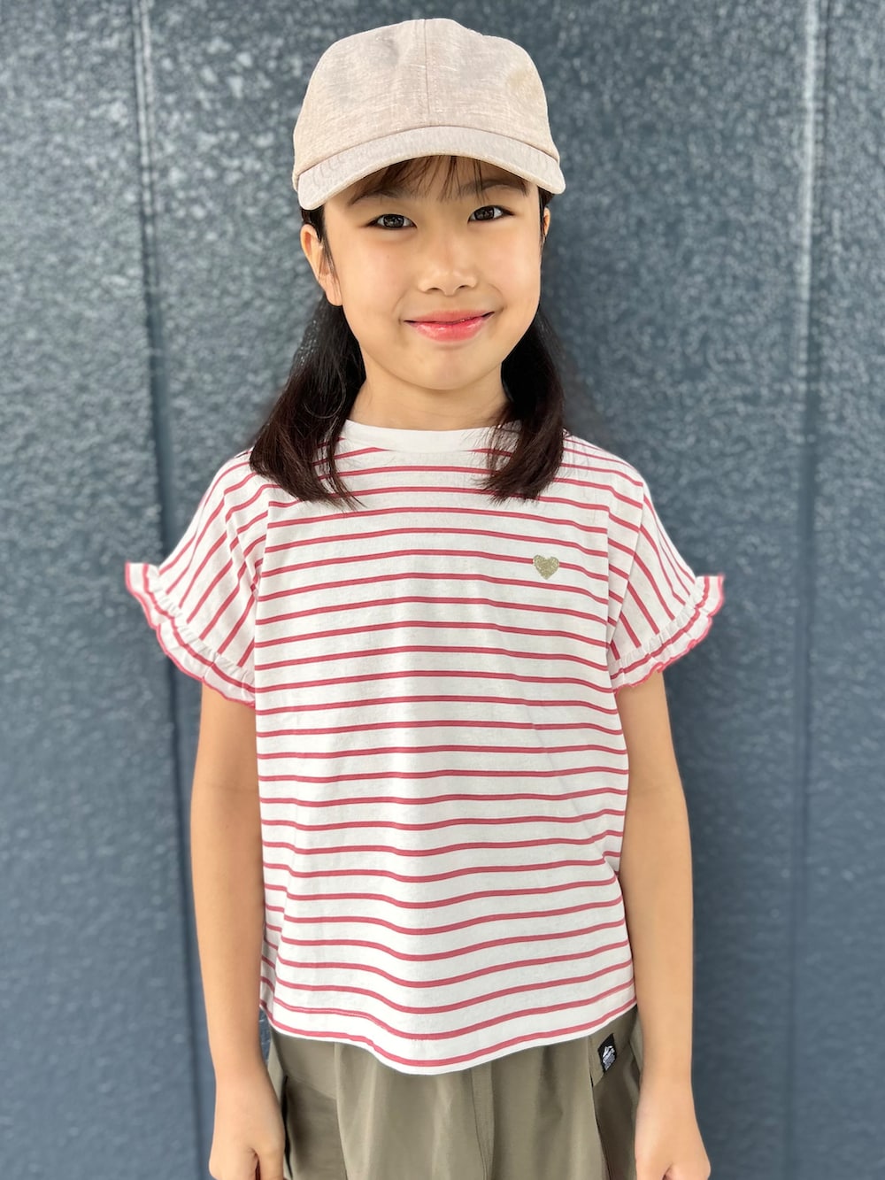 レッド系のTシャツ/カットソー、ブラウン系のスカート、ベージュ系のキャップを着用したキッズの夏コーディネートの6枚目の写真