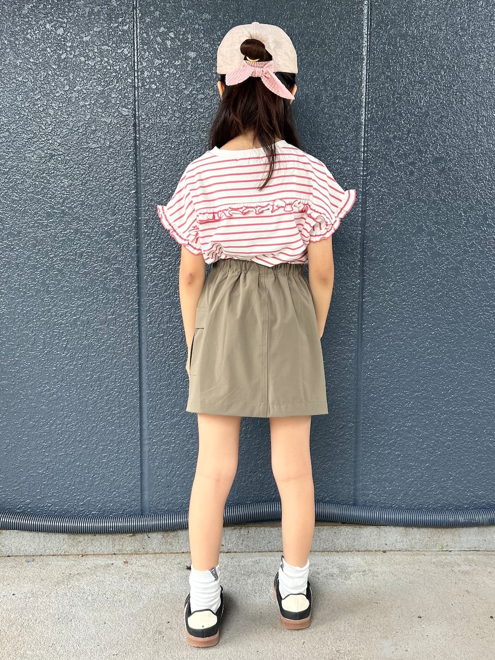 レッド系のTシャツ/カットソー、ブラウン系のスカート、ベージュ系のキャップを着用したキッズの夏コーディネートの3枚目の写真
