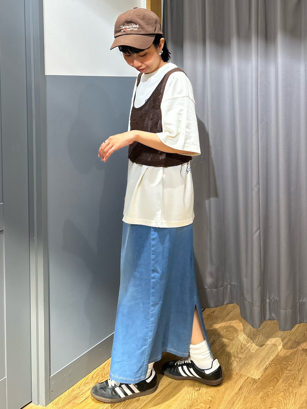 ブラウン系のベスト、ブルー系のスカート、ブラウン系のキャップを着用したレディースの夏コーディネートの2枚目の写真