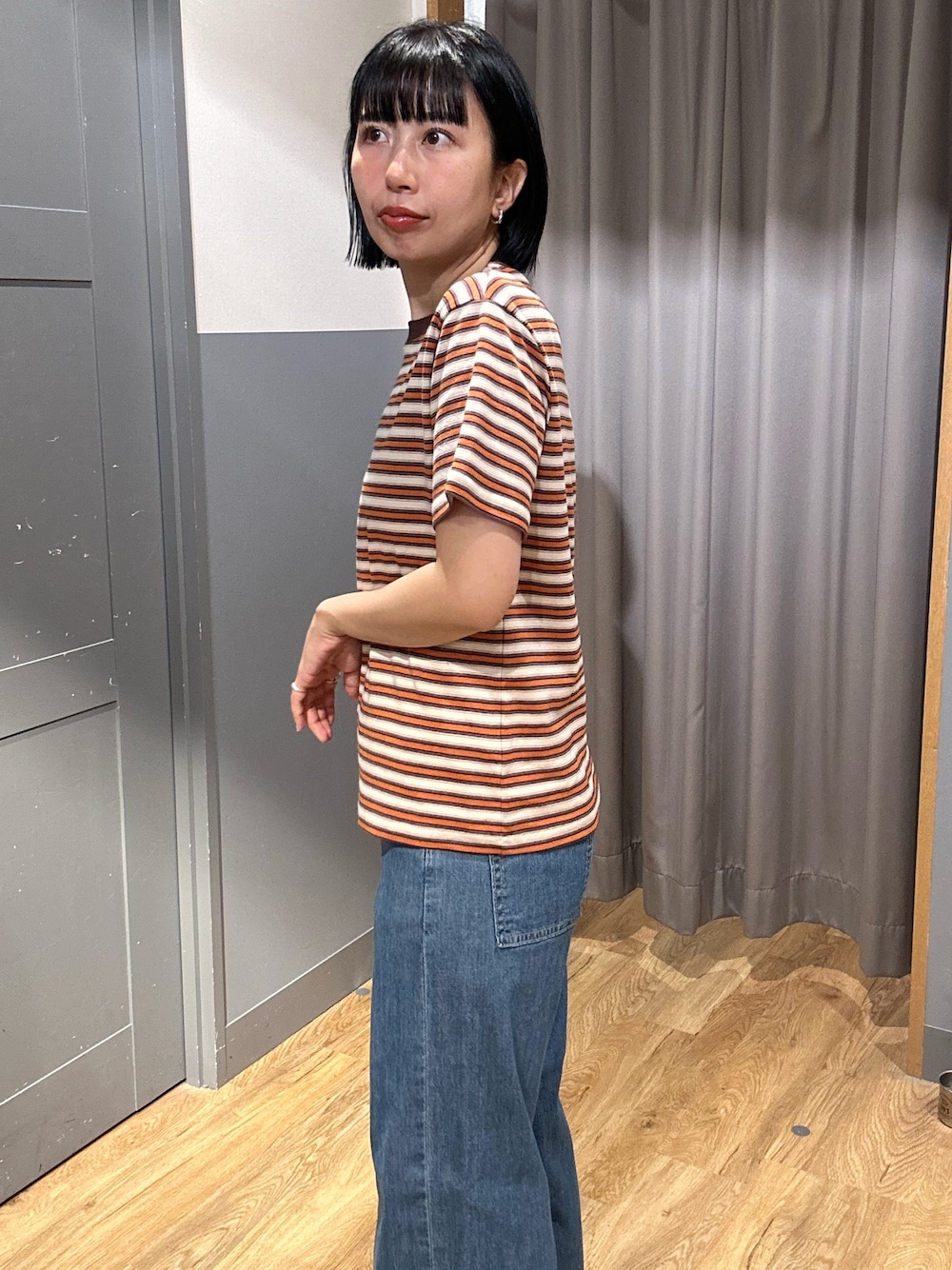 オレンジ系のTシャツ/カットソー、ブラウン系のベスト、ブルー系のデニムパンツを着用したレディースの春コーディネートの6枚目の写真