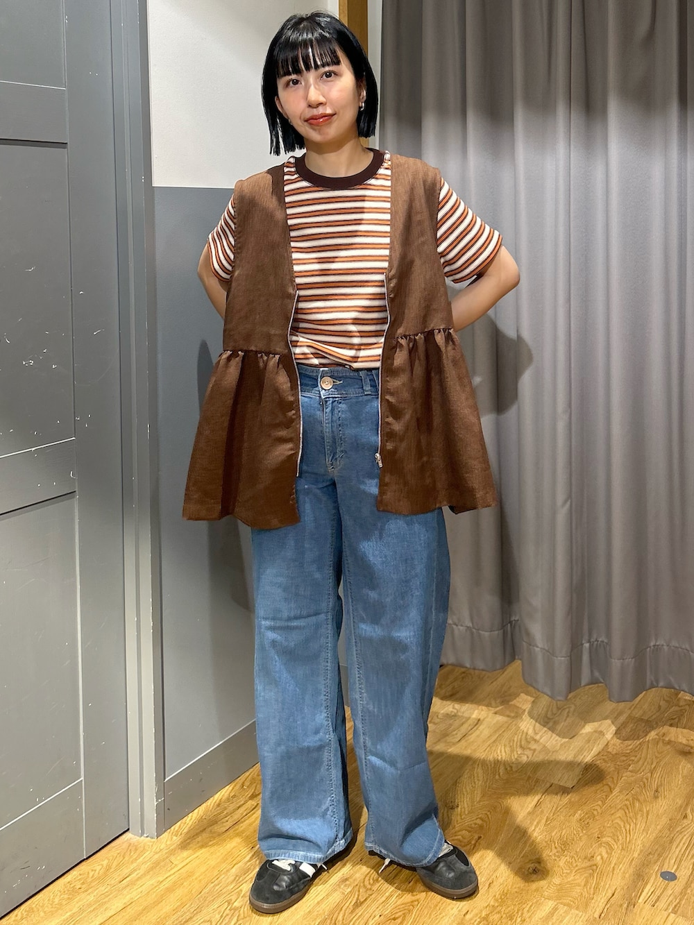 オレンジ系のTシャツ/カットソー、ブラウン系のベスト、ブルー系のデニムパンツを着用したレディースの春コーディネートの2枚目の写真
