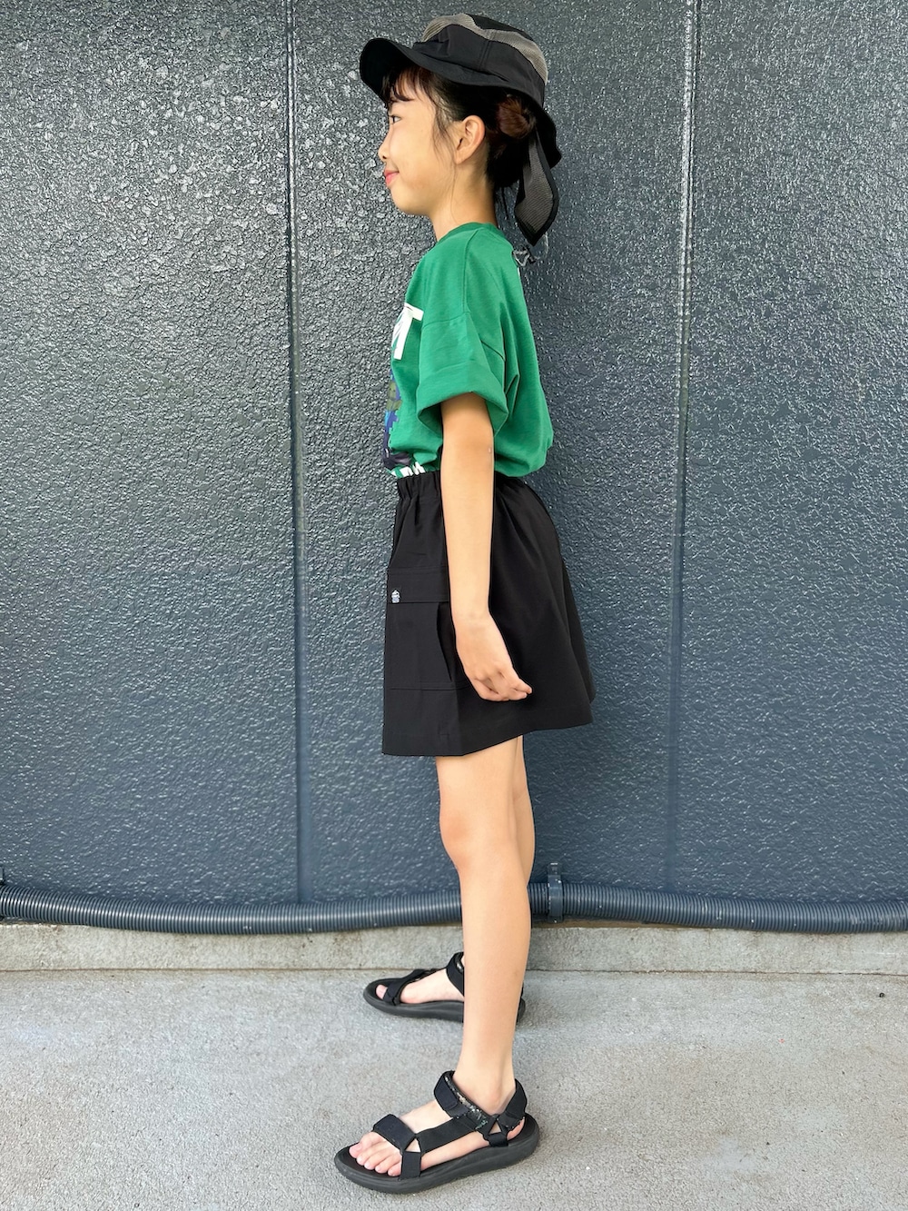グリーン系のTシャツ/カットソー、ブラック系のスカート、ブラック系のハットを着用したキッズの夏コーディネートの2枚目の写真