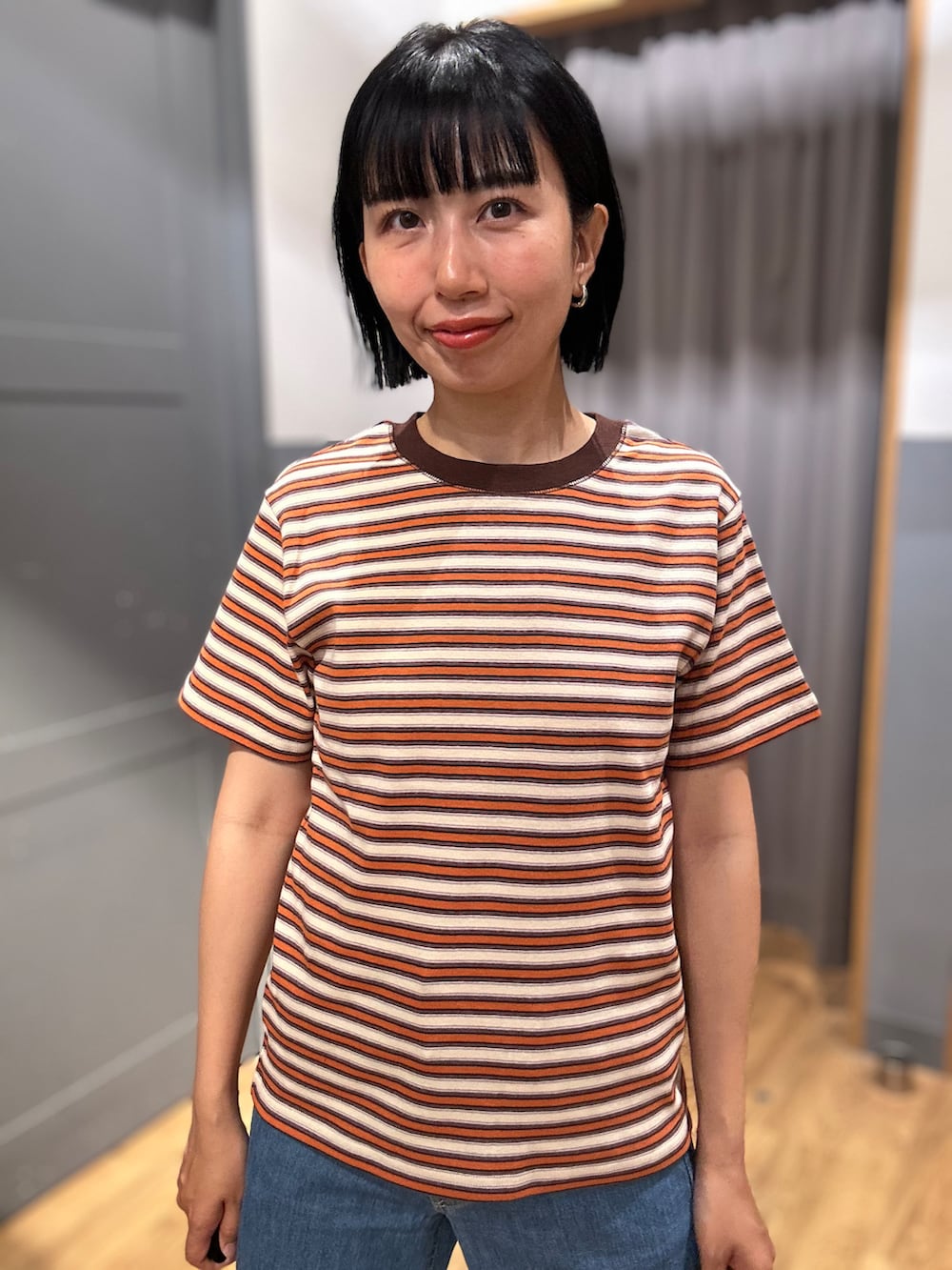 オレンジ系のTシャツ/カットソー、ブラウン系のベスト、ブルー系のデニムパンツを着用したレディースの春コーディネートの5枚目の写真
