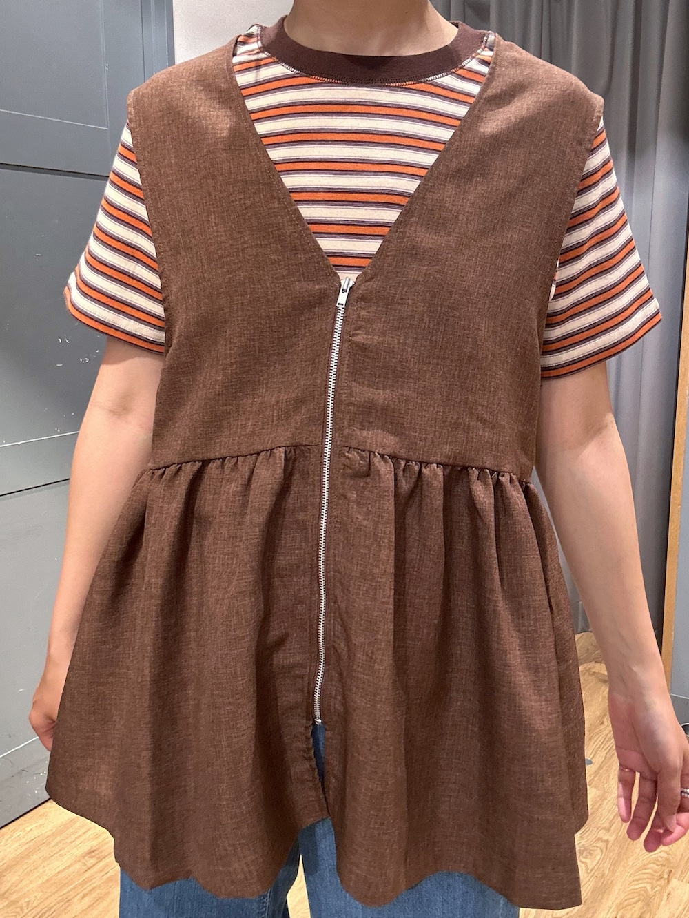 オレンジ系のTシャツ/カットソー、ブラウン系のベスト、ブルー系のデニムパンツを着用したレディースの春コーディネートの7枚目の写真