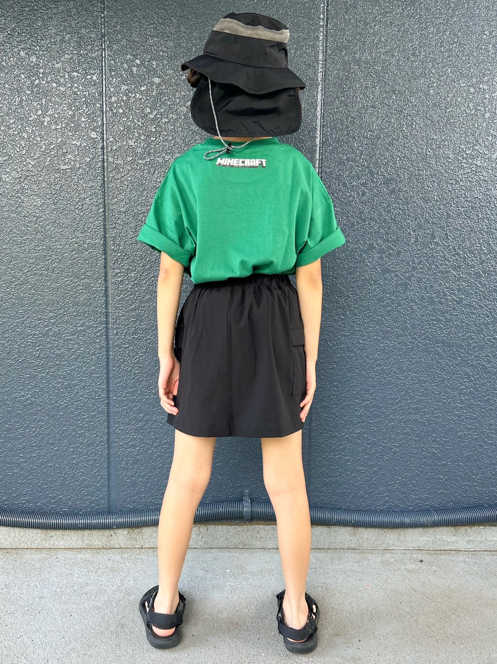 グリーン系のTシャツ/カットソー、ブラック系のスカート、ブラック系のハットを着用したキッズの夏コーディネートの3枚目の写真