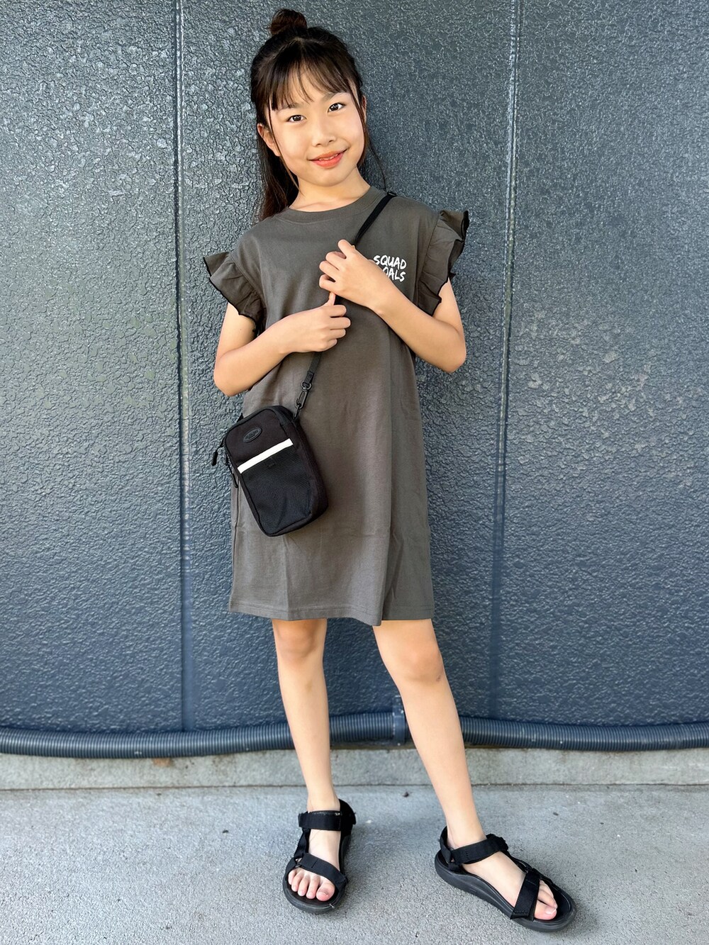 ブラック系のワンピース、ブラック系のショルダーバッグを着用したキッズの夏コーディネートの2枚目の写真