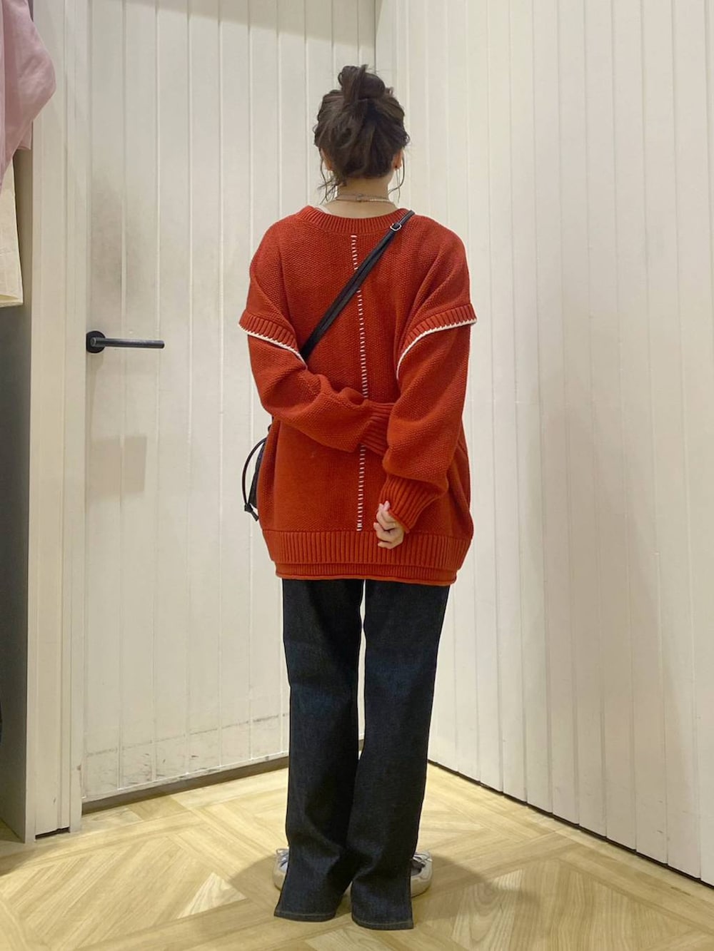 レッド系のニット/セーター、ブルー系のデニムパンツ、ブラック系のショルダーバッグを着用したレディースの秋コーディネートの3枚目の写真