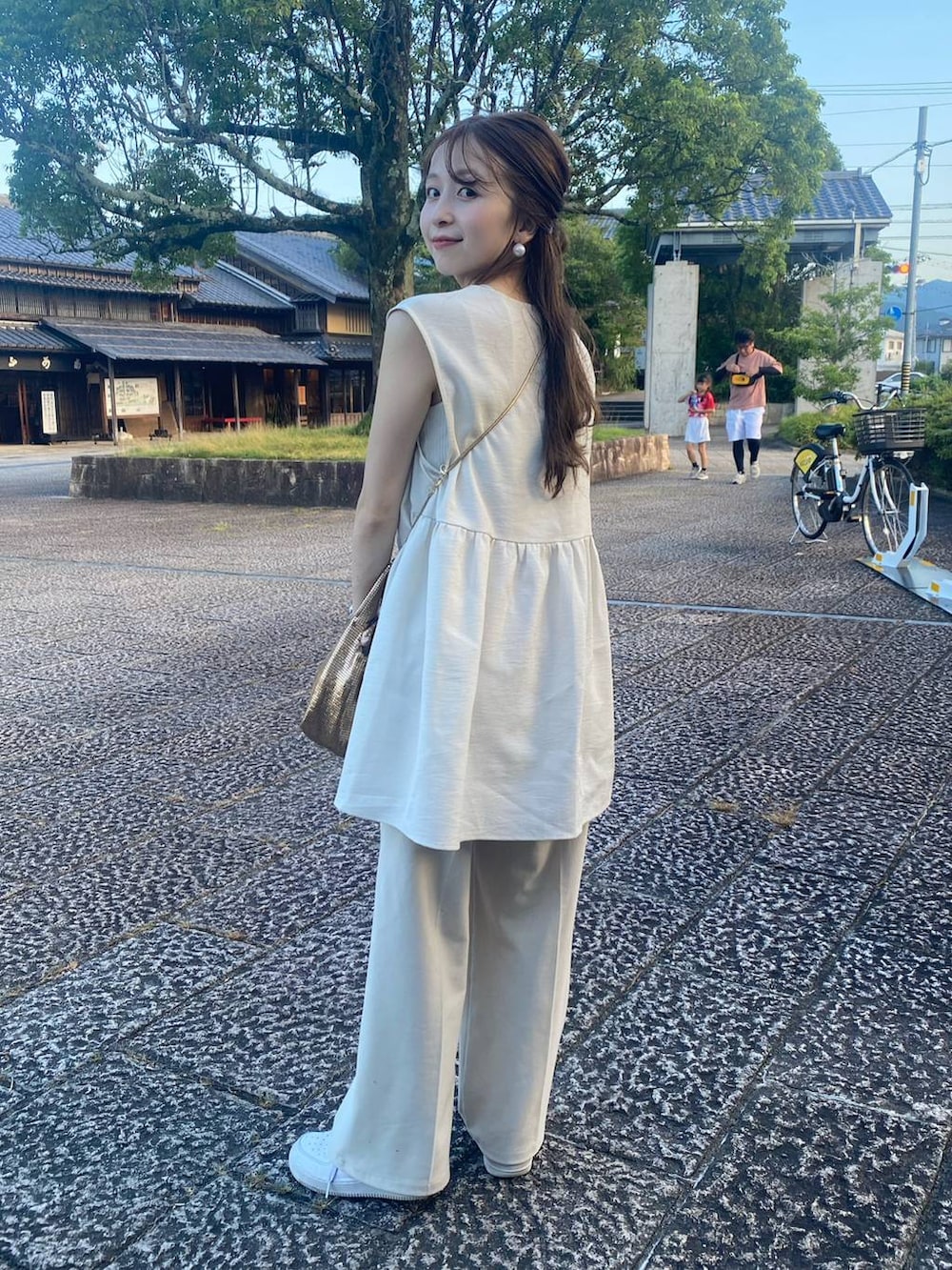 ゴールド系のショルダーバッグ、ホワイト系のベスト、ホワイト系のキャミソールを着用したレディースの夏コーディネートの3枚目の写真