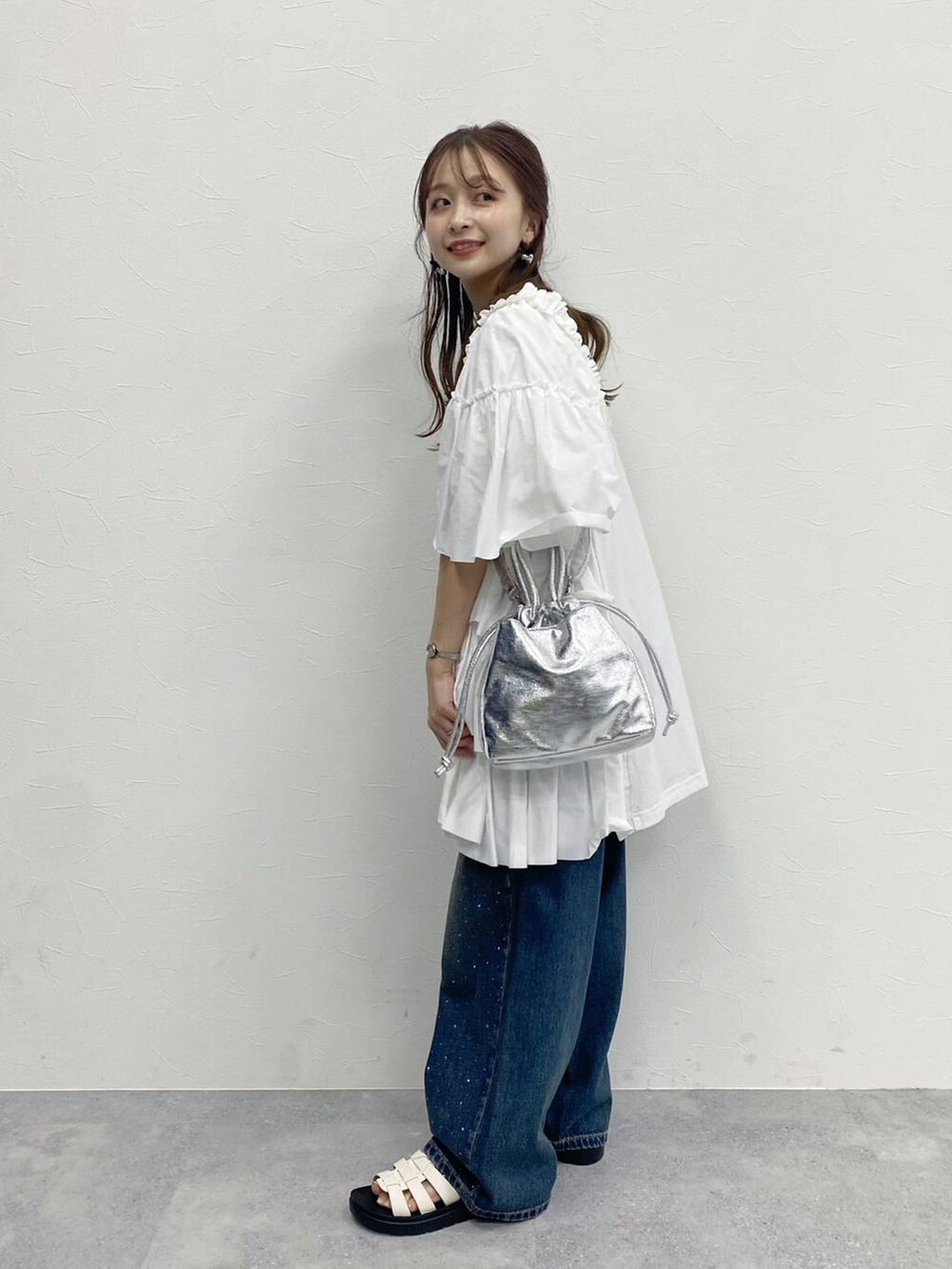 ブルー系のデニムパンツ、ホワイト系のスニーカー、シルバー系のハンドバッグを着用したレディースの春コーディネートの3枚目の写真