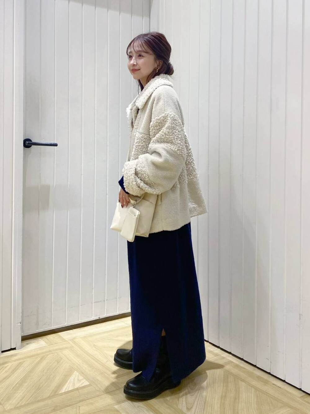 ブラック系のブーツ、ブルー系のワンピース、ホワイト系のショルダーバッグを着用したレディースの冬コーディネートの2枚目の写真