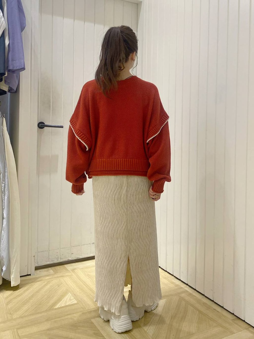 レッド系のニット/セーター、ホワイト系のスニーカー、ホワイト系のスカートを着用したレディースの秋コーディネートの2枚目の写真