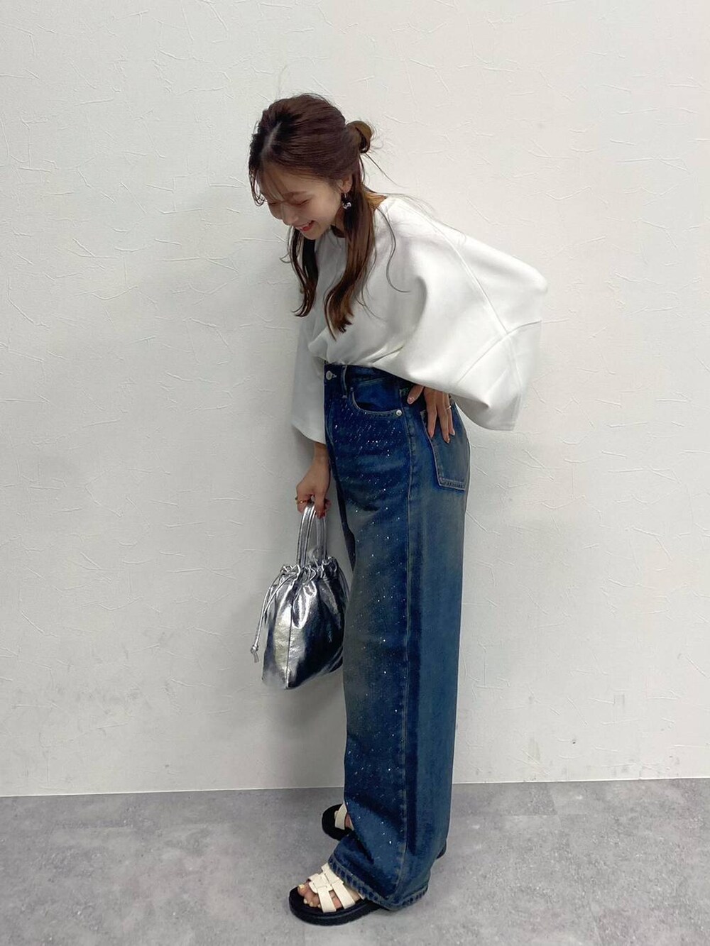 ブルー系のデニムパンツ、ホワイト系のスニーカー、シルバー系のハンドバッグを着用したレディースの春コーディネートの3枚目の写真