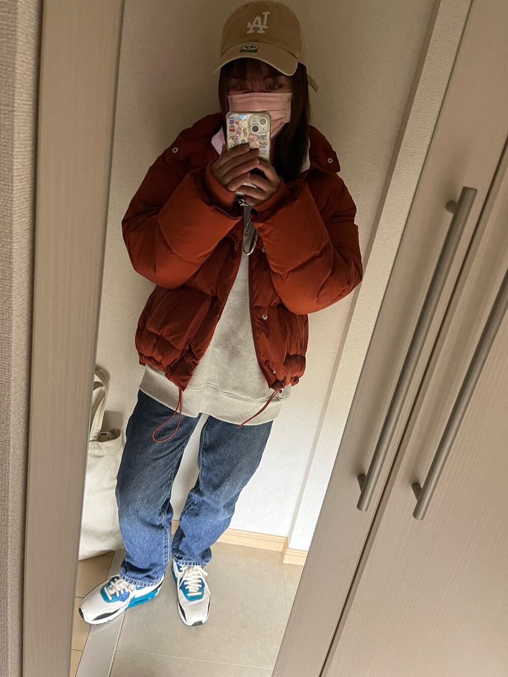 オレンジ系のダウンジャケット/コート、グレー系のスウェット、ブルー系のデニムパンツを着用したレディースの冬コーディネートの2枚目の写真