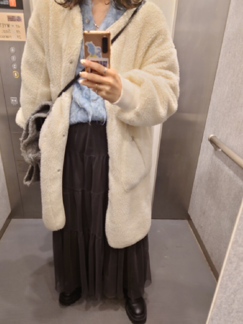 ホワイト系のノーカラーコート、グリーン系のスカート、ブルー系のカーディガン/ボレロを着用したレディースの冬コーディネートの2枚目の写真