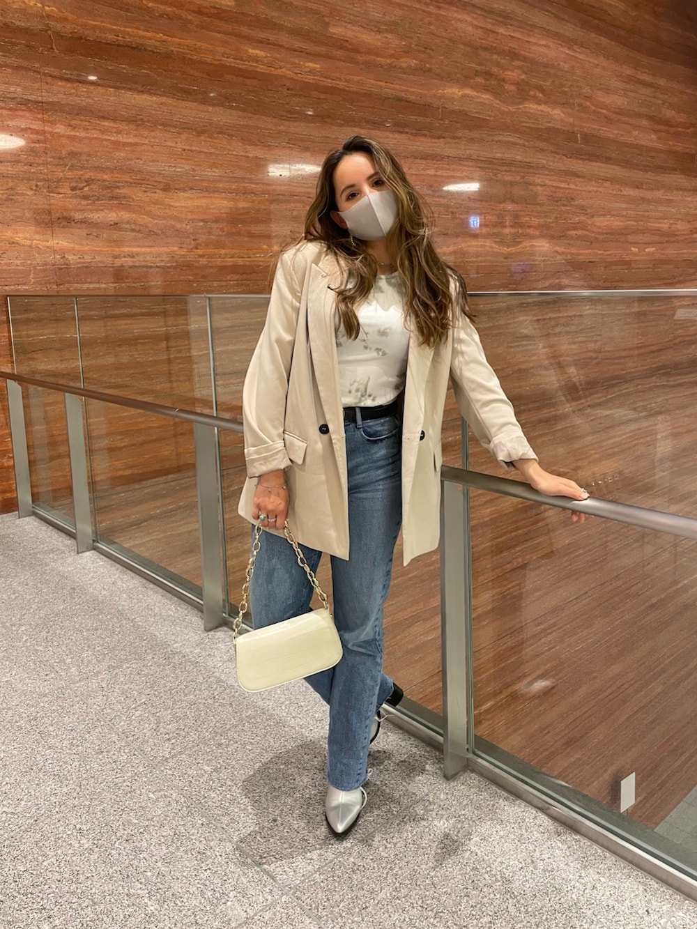 ブルー系のデニムパンツ、ベージュ系のテーラードジャケット、ベージュ系のハンドバッグを着用したレディースの春コーディネートの2枚目の写真