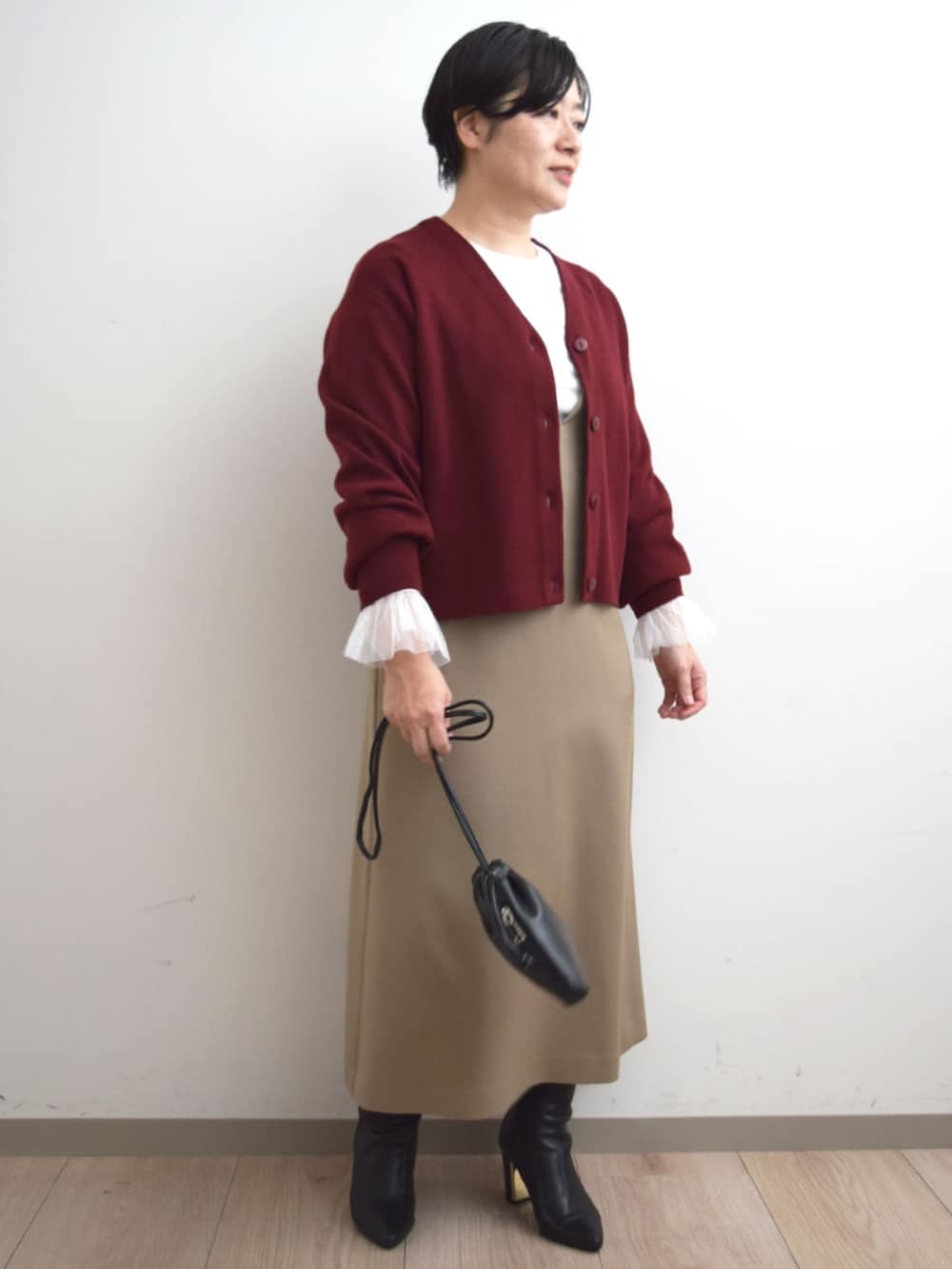 レッド系のカーディガン/ボレロ、ホワイト系のTシャツ/カットソー、ベージュ系のジャンパースカートを着用したレディースの秋コーディネートの4枚目の写真