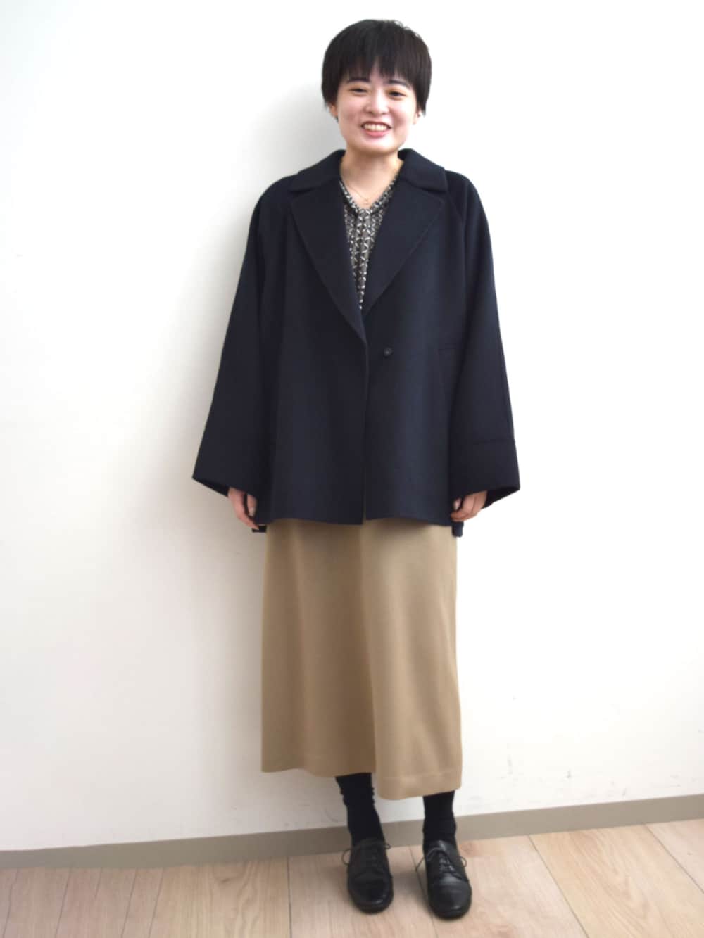 ベージュ系のジャンパースカート、ブラウン系のTシャツ/カットソー、ブルー系のノーカラーコートを着用したレディースの秋コーディネートの4枚目の写真