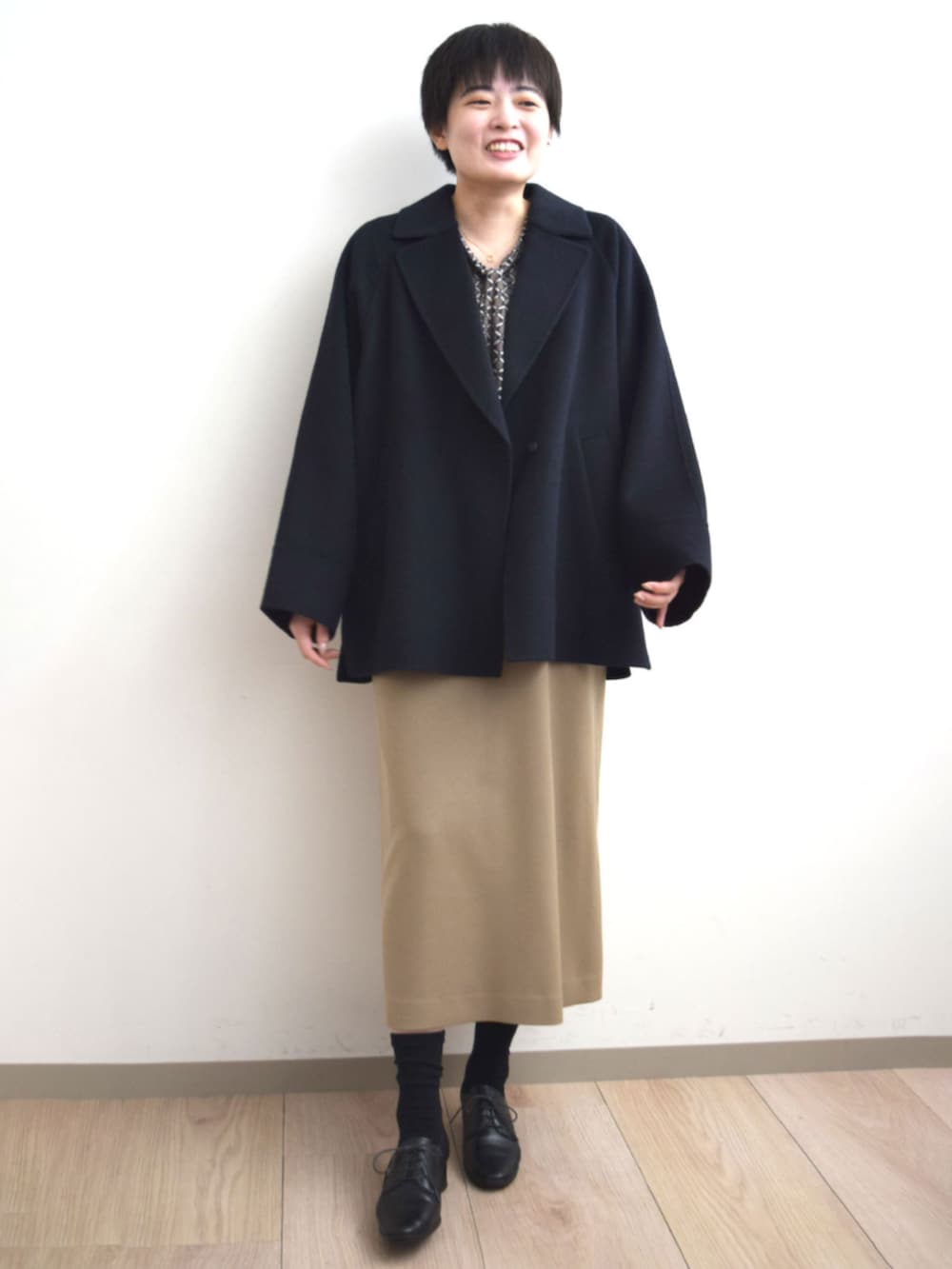 ベージュ系のジャンパースカート、ブラウン系のTシャツ/カットソー、ブルー系のノーカラーコートを着用したレディースの秋コーディネートの2枚目の写真