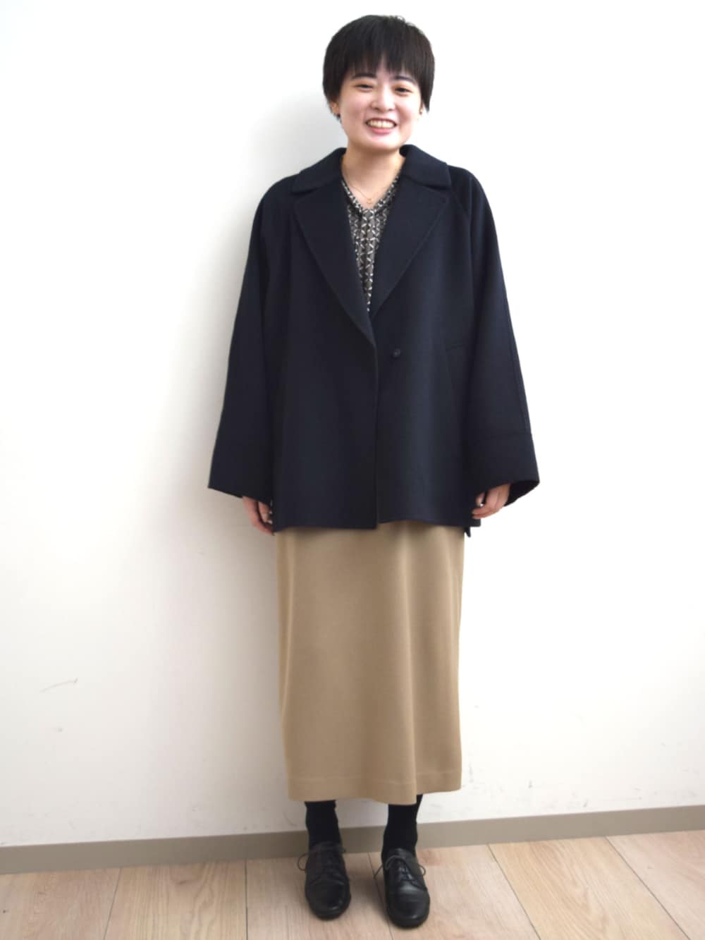 ベージュ系のジャンパースカート、ブラウン系のTシャツ/カットソー、ブルー系のノーカラーコートを着用したレディースの秋コーディネートの3枚目の写真