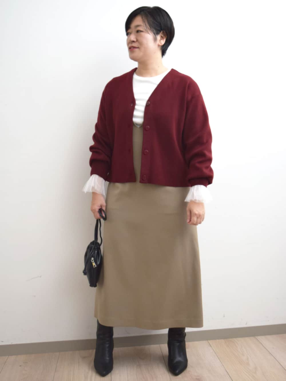 レッド系のカーディガン/ボレロ、ホワイト系のTシャツ/カットソー、ベージュ系のジャンパースカートを着用したレディースの秋コーディネートの3枚目の写真