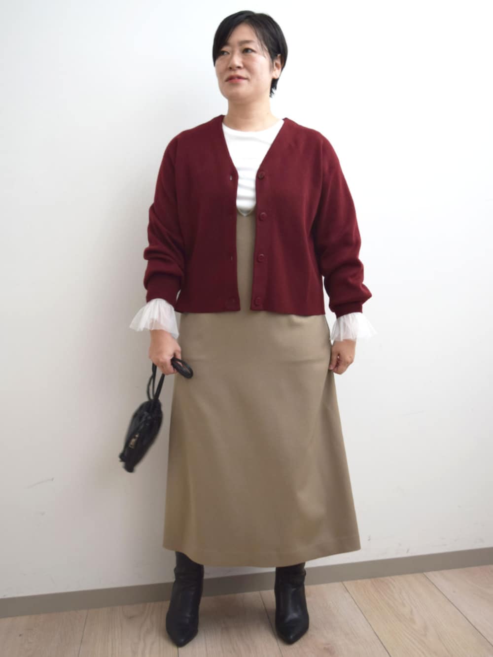 レッド系のカーディガン/ボレロ、ホワイト系のTシャツ/カットソー、ベージュ系のジャンパースカートを着用したレディースの秋コーディネートの2枚目の写真