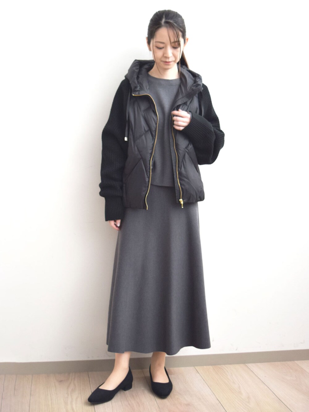 ブラック系のダウンジャケット/コート、グレー系のニット/セーター、グレー系のスカートを着用したレディースの秋コーディネートの2枚目の写真