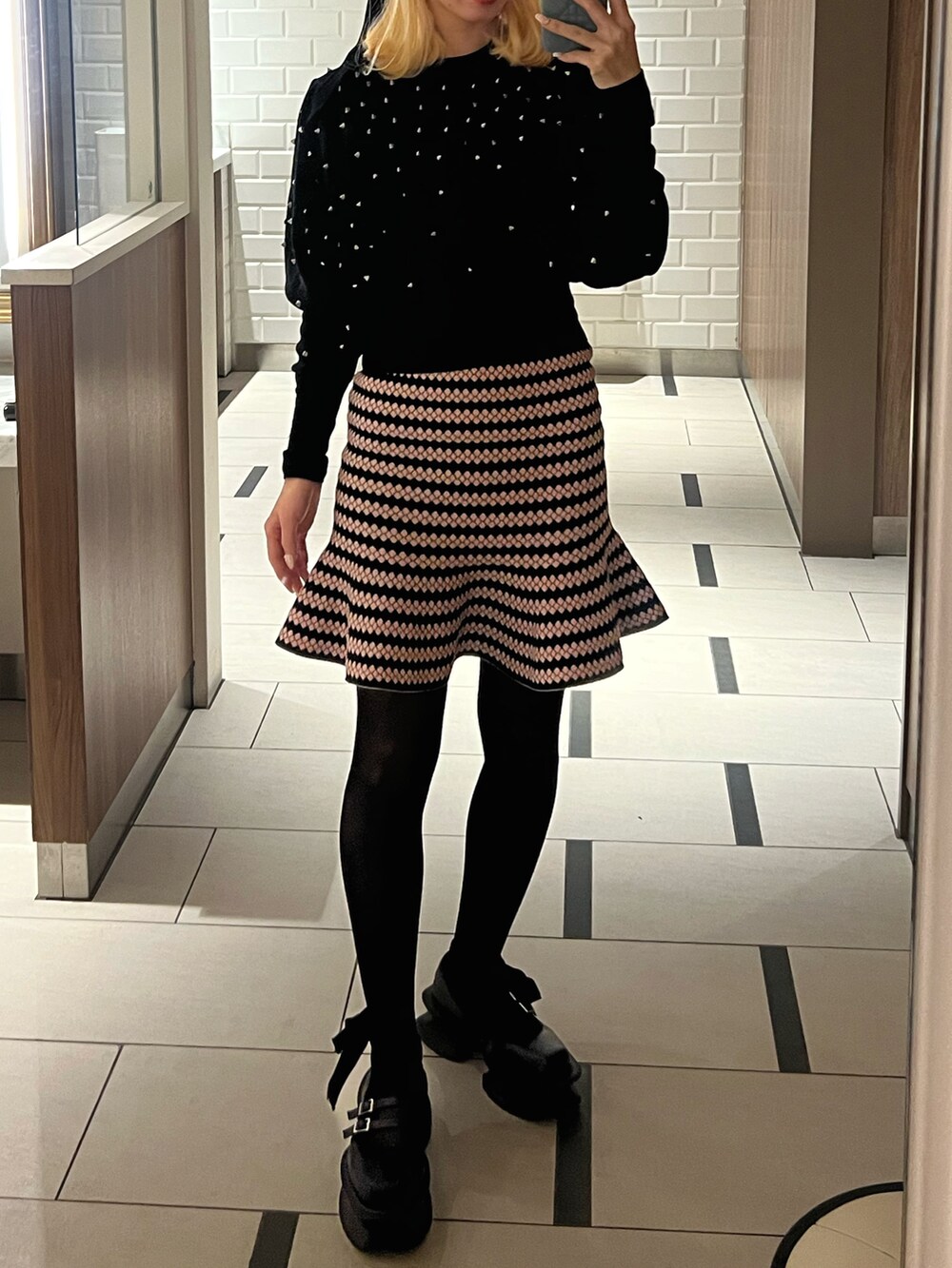 ピンク系のスカート、ブラック系のニット/セーター、ブラック系のローファーを着用したレディースの冬コーディネートの2枚目の写真