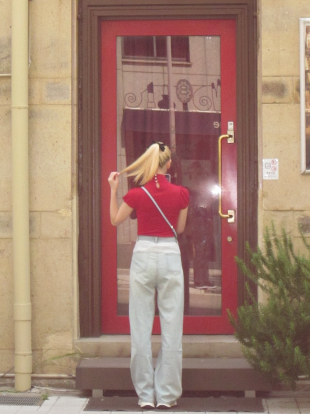 ブルー系のデニムパンツ、レッド系のトップス、ブラウン系のショルダーバッグを着用したレディースの春コーディネートの3枚目の写真