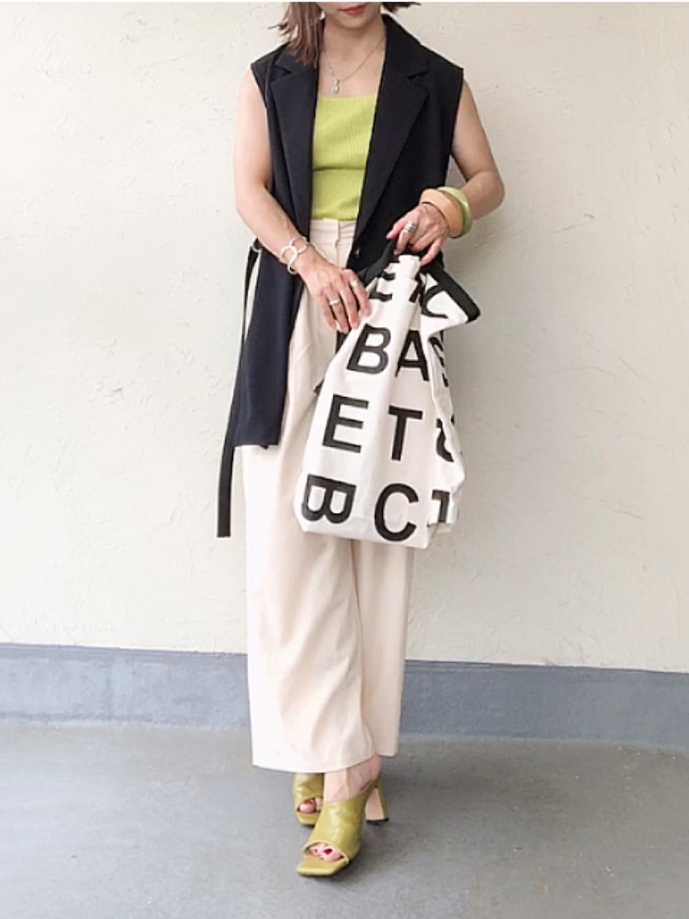 ブルー系のベスト、イエロー系のタンクトップ、ホワイト系のトートバッグを着用したレディースの夏コーディネートの2枚目の写真