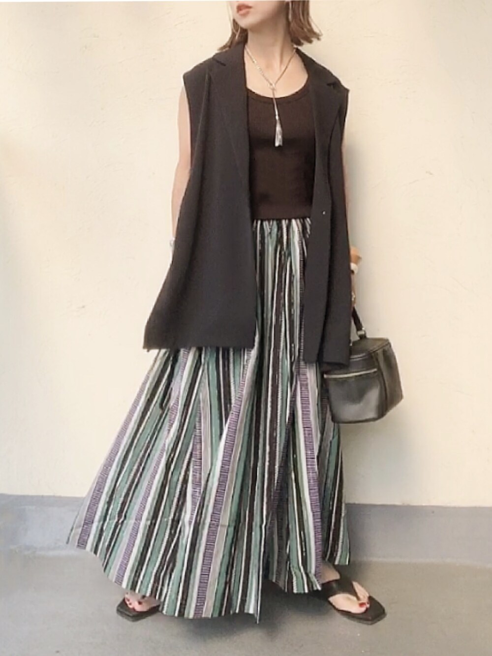 ブルー系のベスト、グリーン系のスカート、ブラック系のハンドバッグを着用したレディースの夏コーディネートの3枚目の写真