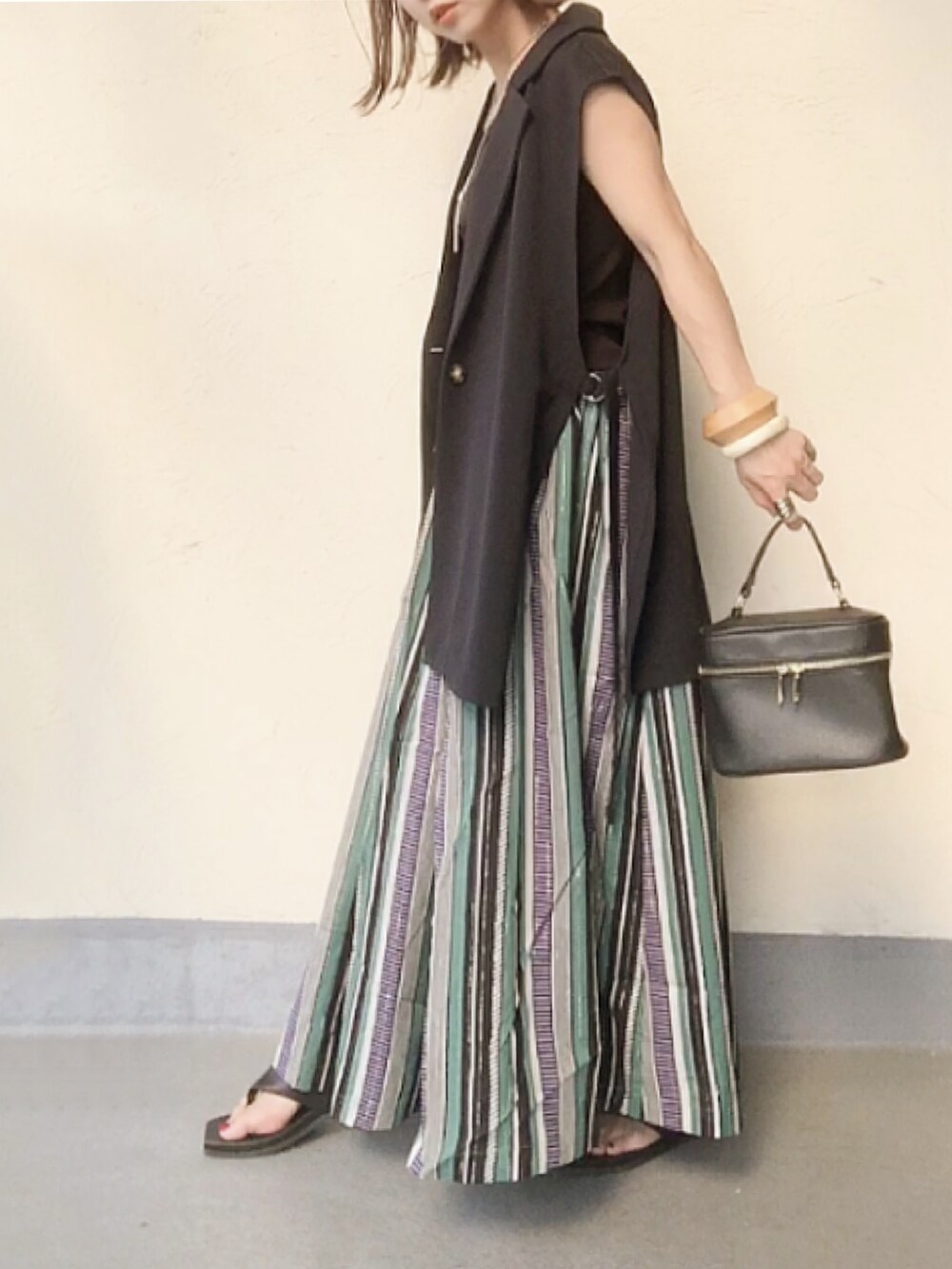 ブルー系のベスト、グリーン系のスカート、ブラック系のハンドバッグを着用したレディースの夏コーディネートの2枚目の写真