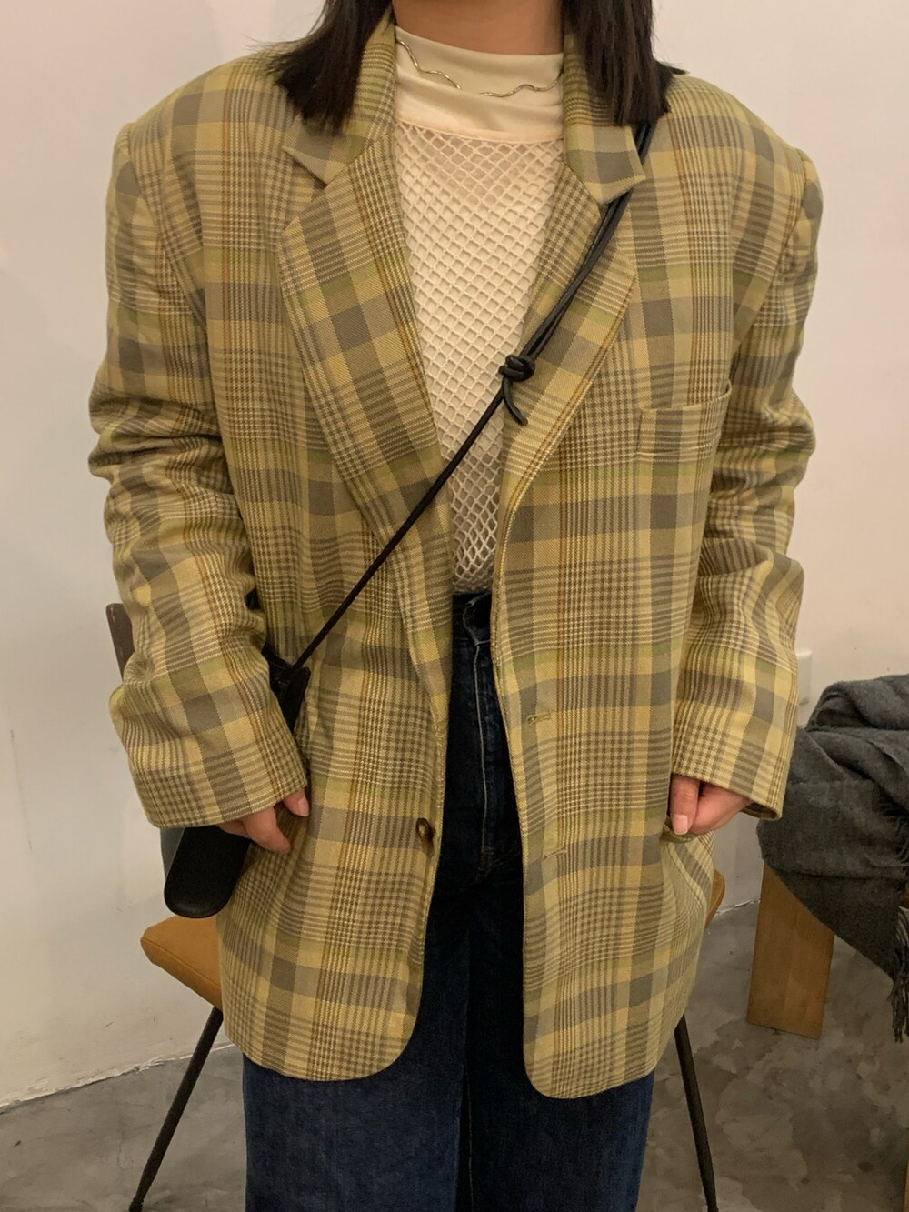 イエロー系のテーラードジャケット、ブルー系のデニムパンツ、ブラック系のハンドバッグを着用したレディースの冬コーディネートの3枚目の写真