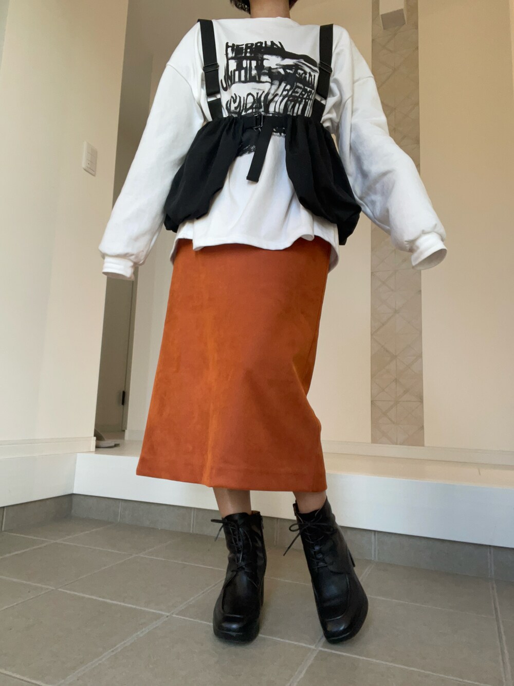 オレンジ系のスカート、ホワイト系のTシャツ/カットソー、ブラック系のベストを着用したレディースの冬コーディネートの4枚目の写真