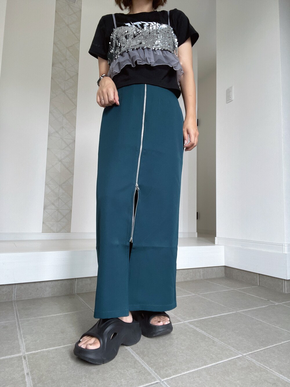 ブラック系のサンダル、グリーン系のスカート、シルバー系のキャミソールを着用したレディースの夏コーディネートの2枚目の写真