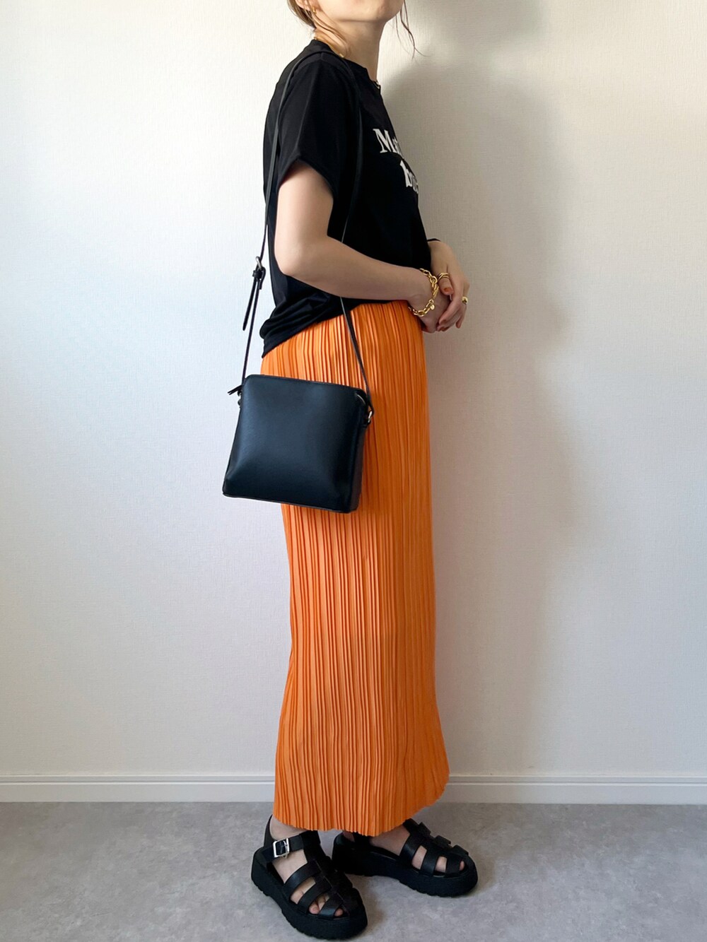 オレンジ系のスカート、ブラック系のTシャツ/カットソー、ブラック系のショルダーバッグを着用したレディースの夏コーディネートの2枚目の写真