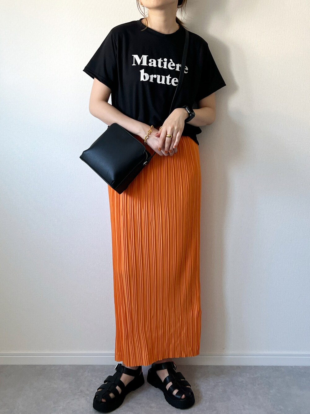 オレンジ系のスカート、ブラック系のTシャツ/カットソー、ブラック系のショルダーバッグを着用したレディースの夏コーディネートの3枚目の写真
