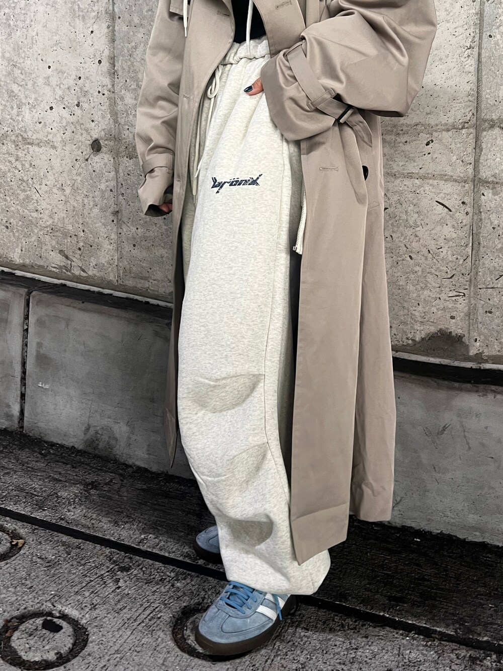 ブルー系のスニーカー、ベージュ系のトレンチコート、グレー系のスウェットパンツを着用したレディースの秋コーディネートの5枚目の写真