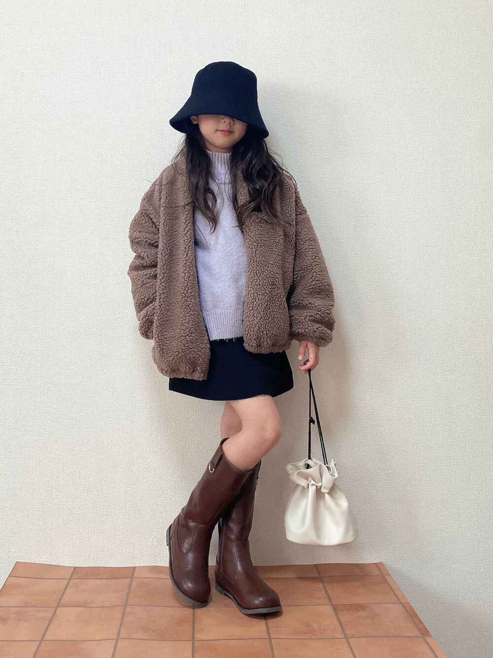 ブラウン系のブルゾン、ブラウン系のブーツ、ホワイト系のハンドバッグを着用したキッズの冬コーディネートの2枚目の写真