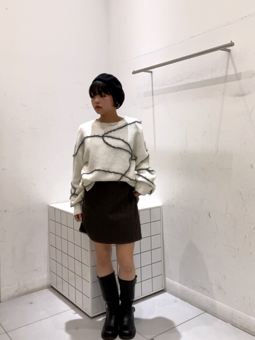 ホワイト系のニット/セーター、ブラウン系のスカート、ブラック系のブーツを着用したレディースの秋コーディネートの2枚目の写真