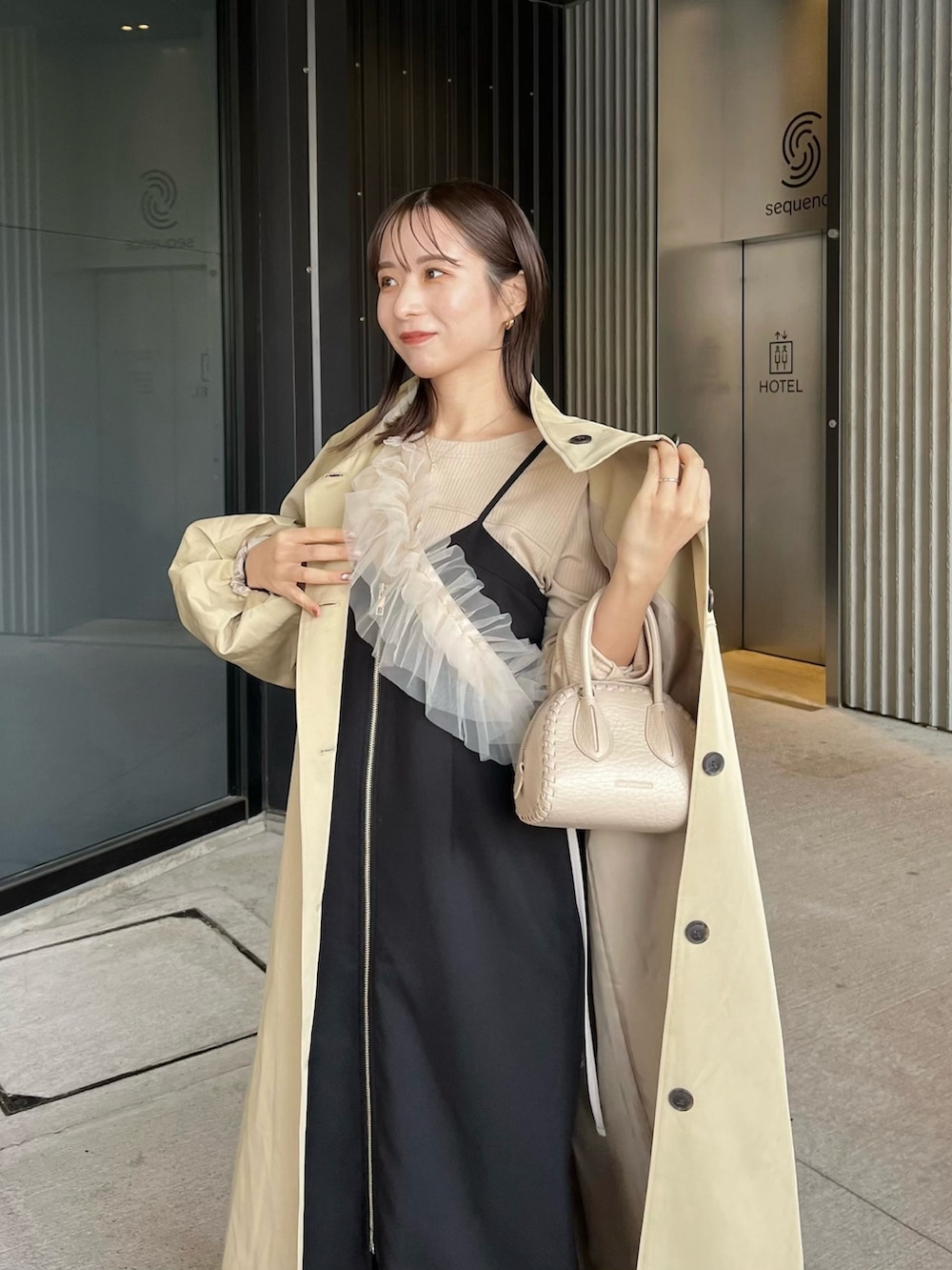 ベージュ系のTシャツ/カットソー、ブラック系のワンピース、ベージュ系のトレンチコートを着用したレディースの冬コーディネートの2枚目の写真