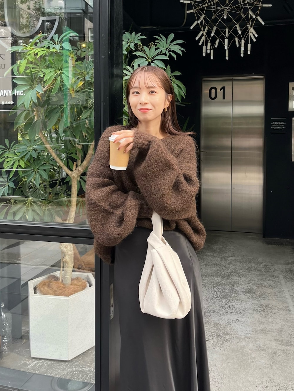 ブラック系のスカート、ブラウン系のニット/セーター、ホワイト系のハンドバッグを着用したレディースの秋コーディネートの4枚目の写真