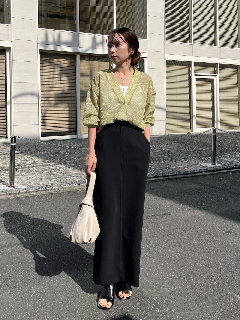 ブラック系のスカート、グリーン系のカーディガン/ボレロ、ホワイト系のハンドバッグを着用したレディースの春コーディネートの2枚目の写真
